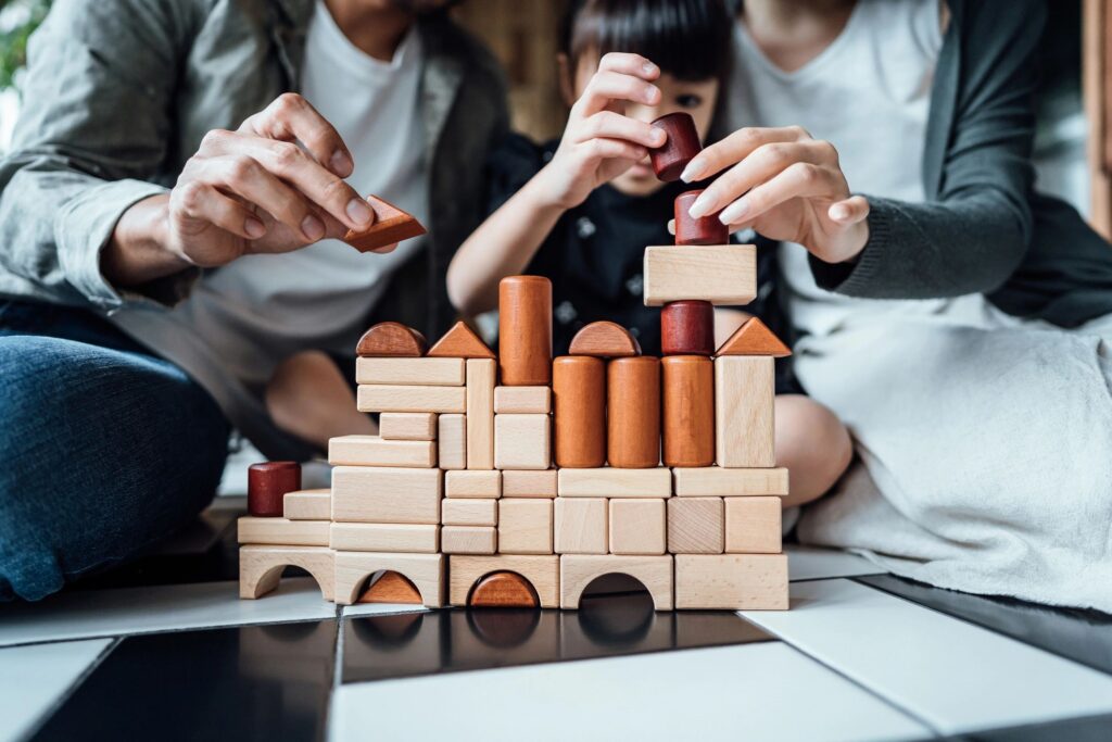 Close up of joyful young Asian family sitting on the floor in the living room having fun playing wooden building blocks with daughter together at home