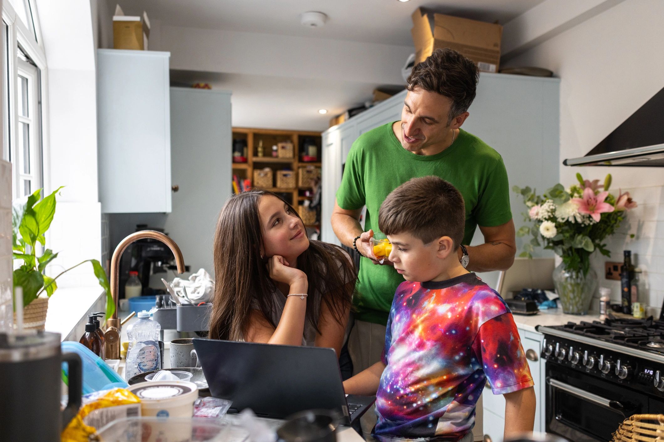 Parent and children learning together at a kitchen table with a laptop