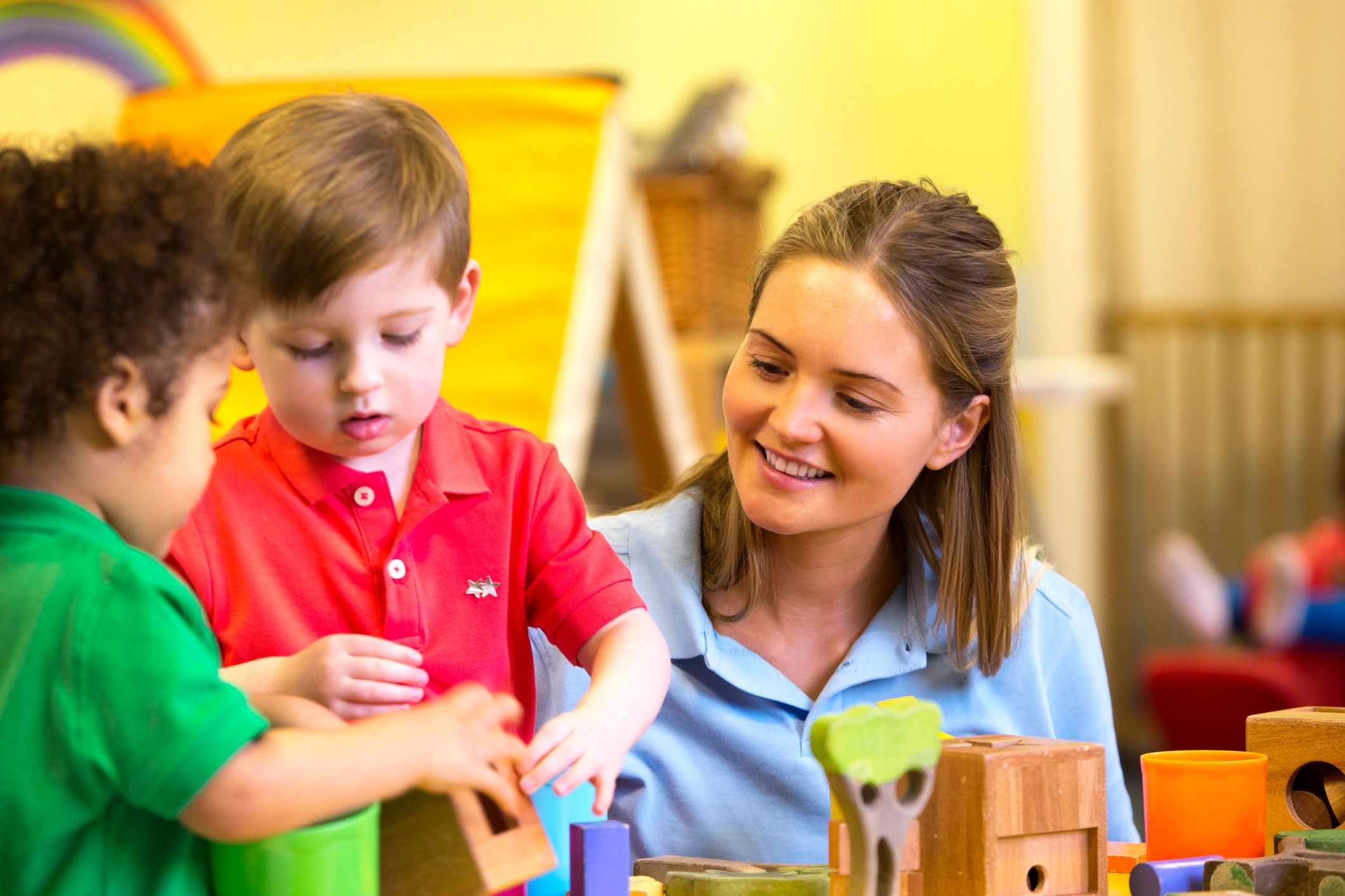 Nursery teacher supporting children as they play and learn with building blocks